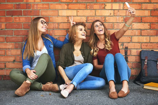 Rendere ricordi del campus. Girato di tre studenti universitari sorridenti che si fanno un selfie insieme mentre si siedono fuori nel campus. — Foto Stock