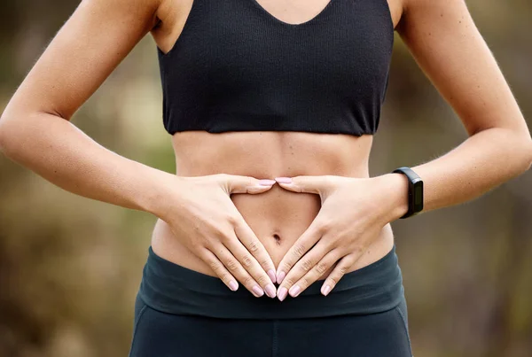 Enamórate de un ser saludable. Primer plano de una mujer irreconocible haciendo una forma de corazón con las manos en el estómago mientras hace ejercicio al aire libre. —  Fotos de Stock