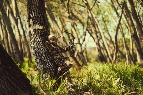 Es un gran tirador. Tiro de un lindo niño en camuflaje jugando con su arco y flecha en el bosque. —  Fotos de Stock
