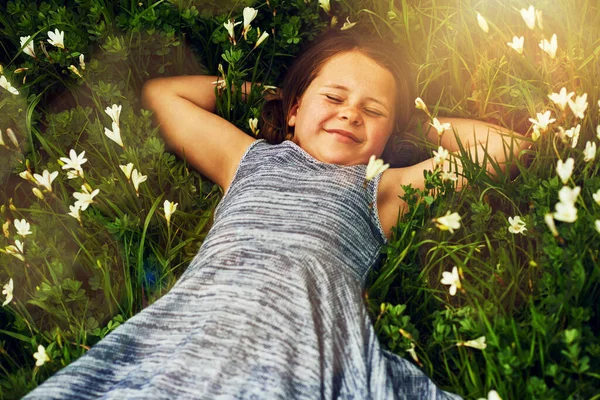 Haciendo amistad con las flores. Shot de una linda niña mintiendo en un campo de flores silvestres fuera. — Foto de Stock