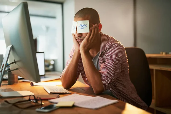 Quando ficar acordado é quase impossível. Tiro cortado de um jovem designer trabalhando tarde em um escritório com notas adesivas cobrindo seus olhos. — Fotografia de Stock