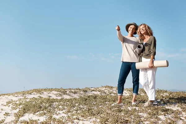 Ce zici de asta? Full lungime shot de două femei mature atractive în picioare cu lor pe plaja. — Fotografie, imagine de stoc