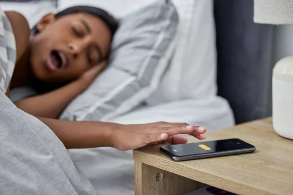 Im snoozing this alarm. Shot of a womans alarm on her cellphone going off while she lies in bed.