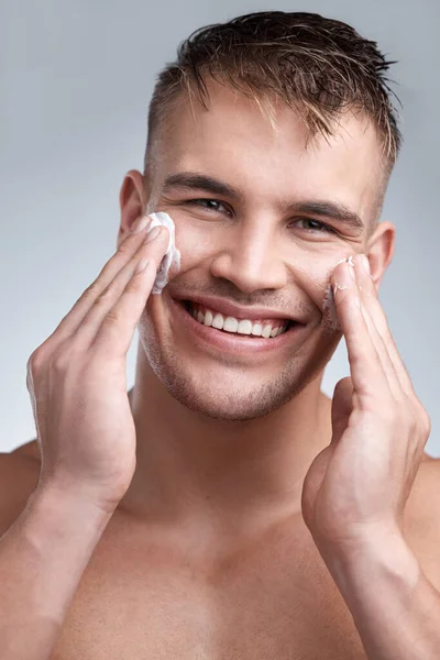 Beauty stained hands. Cropped closeup portrait of an attractive young man applying moisturiser to his face against a grey background. — Stock Photo, Image