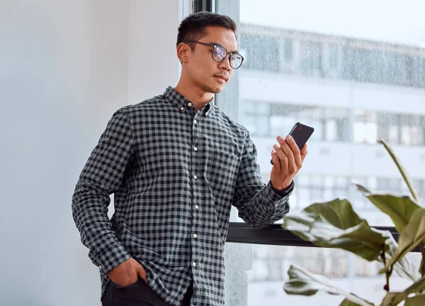 A quick social media break. Shot of a young businessman using a phone in an office.