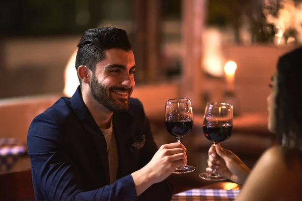 A uma bela noite fora. Tiro de um jovem casal alegre fazendo um brinde comemorativo com copos de vinho enquanto olham nos olhos uns dos outros durante o jantar fora à noite. — Fotografia de Stock