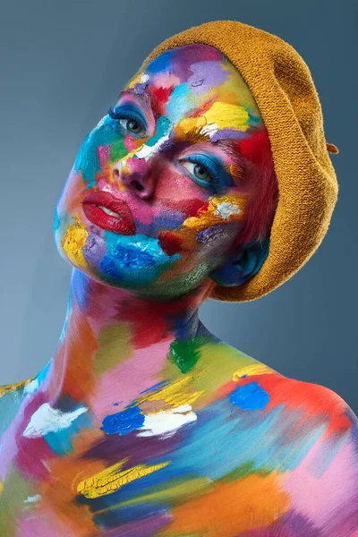 La vita consiste nell'usare l'intera scatola di pastelli. Studio foto di una giovane donna in posa con vernice multicolore sul viso e un cappello francese sulla testa. — Foto Stock