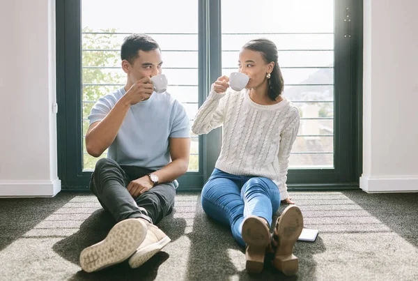 Unsere erste Tasse Tee in unserem neuen Zuhause. Ein junges Paar sitzt in voller Länge in seinem neuen Zuhause zusammen und genießt eine Tasse Tee. — Stockfoto