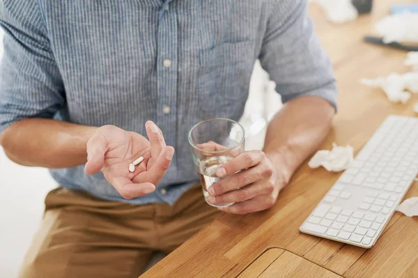 Buscando alívio da dor. Foto de perto de um empresário irreconhecível segurando um copo de água e medicação em um escritório. — Fotografia de Stock