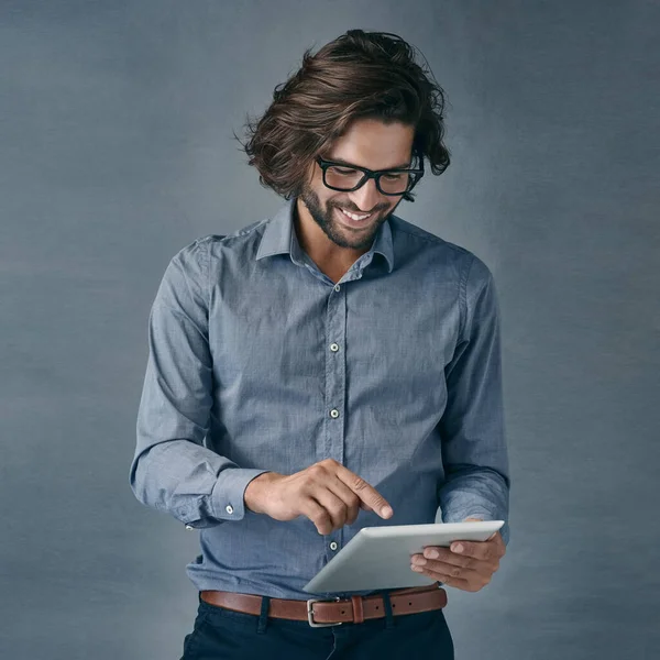 Ik denk dat iedereen er een moet hebben. Foto van een knappe jongeman met een digitale tablet tegen een grijze achtergrond. — Stockfoto