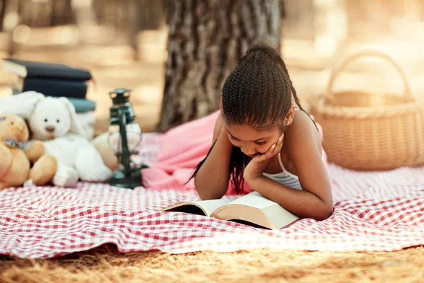 La lecture ouvre de nouveaux mondes pour les enfants. Tourné d'une petite fille lisant un livre avec ses jouets dans les bois. — Photo