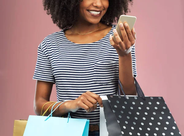 Estoy informando a todo el mundo sobre la nueva tienda. Captura de estudio de una hermosa mujer joven usando su teléfono celular mientras llevaba bolsas de compras. — Foto de Stock