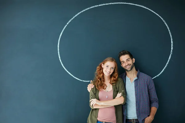 Encircled por seu amor. Retrato de um jovem casal em pé na frente de um quadro negro com um círculo desenhado em torno deles. — Fotografia de Stock
