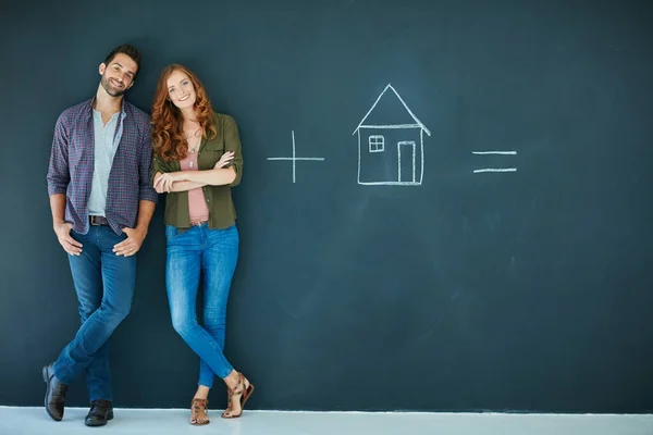 Ingredientes para uma vida feliz. Tiro de um jovem casal em pé na frente de um quadro negro com símbolos escritos nele. — Fotografia de Stock