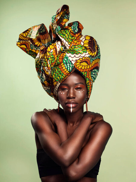 Studio shot of a beautiful young woman wearing a traditional African head wrap against a green background.