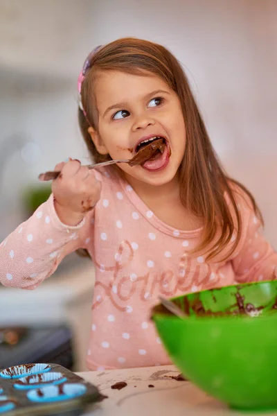 Cibo per i cuochi. Colpo ritagliato di una bambina che lecca la pastella di cupcake da un cucchiaio in cucina. — Foto Stock