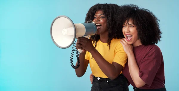 No te calmes, sigue marchando. Captura de estudio de dos mujeres jóvenes usando un megáfono sobre un fondo azul. — Foto de Stock