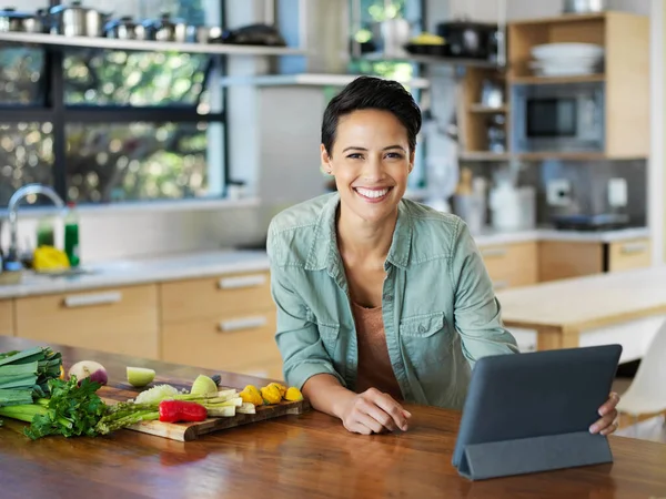 He encontrado la receta perfecta. Retrato de una joven sonriente usando una tableta digital mientras prepara una comida en su cocina. — Foto de Stock