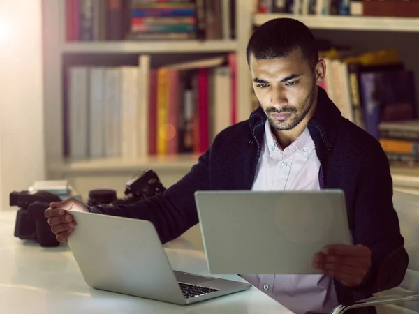 A tecnologia ajuda-o a trabalhar com mais inteligência. Tiro de um jovem fotógrafo focado trabalhando em um laptop e tablet digital em seu escritório em casa no início da noite. — Fotografia de Stock