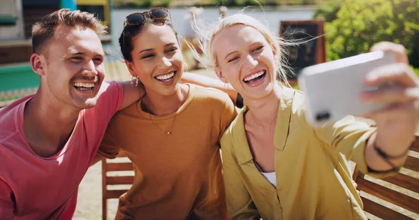 Personne ne me fait sourire plus grand que mes amis. Tournage d'un groupe d'amis prenant des photos à l'extérieur à l'aide d'un smartphone. — Photo