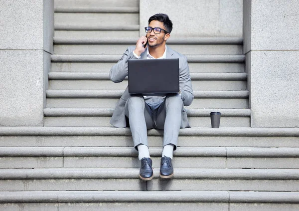 Outra chamada de negócios bem sucedida. Tiro de um jovem empresário usando um laptop enquanto no telefone na cidade. — Fotografia de Stock