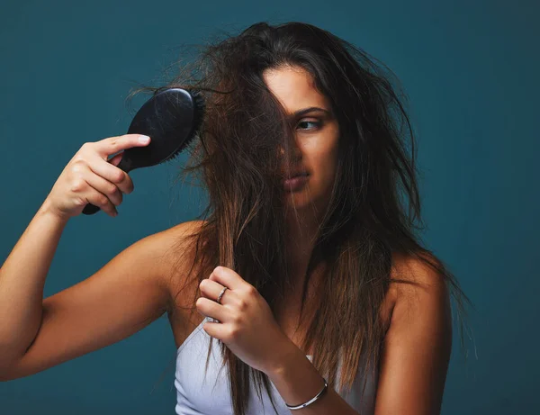 To nie tylko fryzura, to stan umysłu. Studio ujęcie pięknej młodej kobiety trzymającej szczotkę do włosów na niebieskim tle. — Zdjęcie stockowe