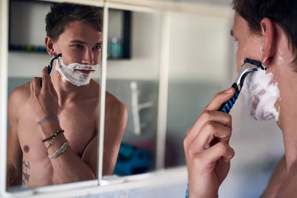 좋은 아침 잘 생겼네. 거울 속에서 자신을 보면서 수염을 면도 하고 있는 젊은 남자의 모습을 찍은 사진. — 스톡 사진