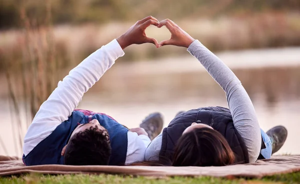 Vamos dormir debaixo das estrelas. Tiro de um jovem casal fazendo um sinal de coração enquanto estava deitado fora. — Fotografia de Stock