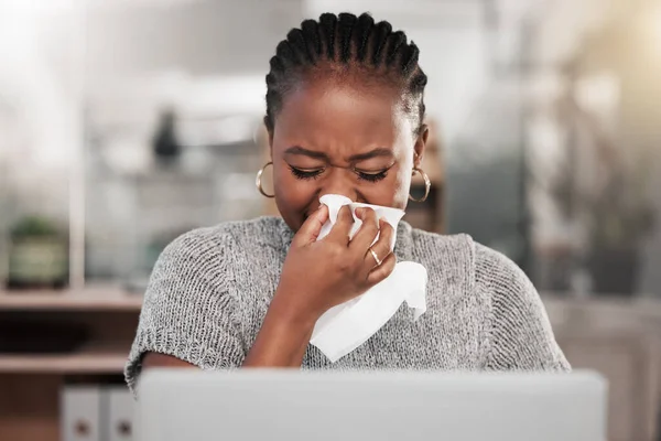 Et soudain, c'était la saison de la grippe. Prise de vue d'une jeune femme d'affaires se mouchant et utilisant un ordinateur portable dans un bureau moderne. — Photo
