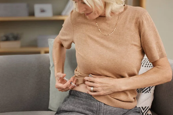 Give life your best shot. Shot of a mature woman injecting herself with insulin on the sofa at home. — Stock Photo, Image