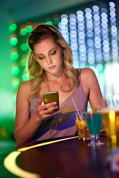Sigo esperando... Fotografía de una mujer joven usando su teléfono celular mientras estaba sentada sola en un club nocturno. — Foto de Stock