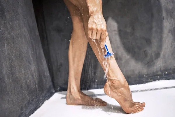 在淋浴间刮胡子比较容易。拍下了一个无法辨认的女人站在家里淋雨刮腿的照片. — 图库照片