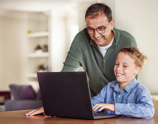 Zorg dat papa 's hulp krijgt. Shot van een schattige kleine jongen zitten en met behulp van een laptop thuis, terwijl zijn vader helpt hem. — Stockfoto