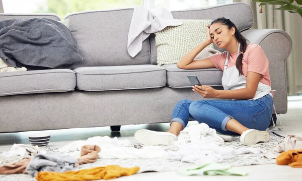 I need some help with these chores. Shot of a woman sitting on the floor with her cellphone in a messy living room. — Stock Photo, Image