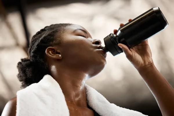 Tijd om te hydrateren. Low angle shot van een aantrekkelijke en atletische jonge vrouw drinken van water tijdens haar training in de sportschool. — Stockfoto