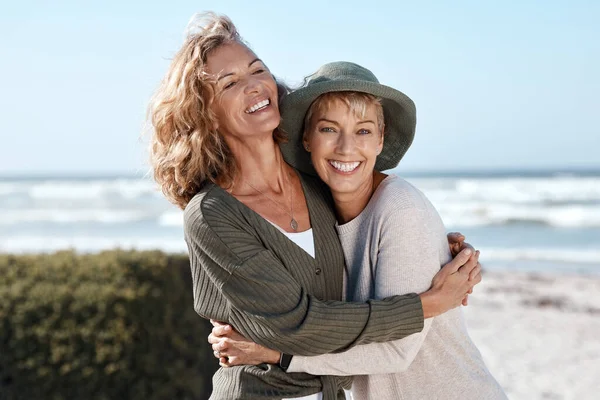Beste vrienden voor het leven. Gesneden schot van twee aantrekkelijke volwassen vrouwen knuffelen terwijl staan op het strand. — Stockfoto
