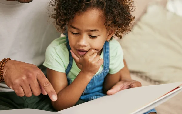 Uwielbia tę książkę. Zdjęcie małej dziewczynki czytającej książkę z rodzicem w domu.. — Zdjęcie stockowe