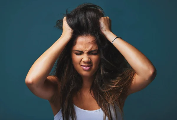 Una decisión tomada con ira es equivocada. Estudio de una hermosa joven con las manos en el pelo posando sobre un fondo azul. — Foto de Stock