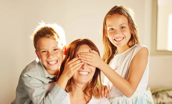 We hebben een verrassing voor je. Schot van twee schattige kinderen band met hun moeder thuis en het bedekken van haar ogen om haar te verrassen. — Stockfoto