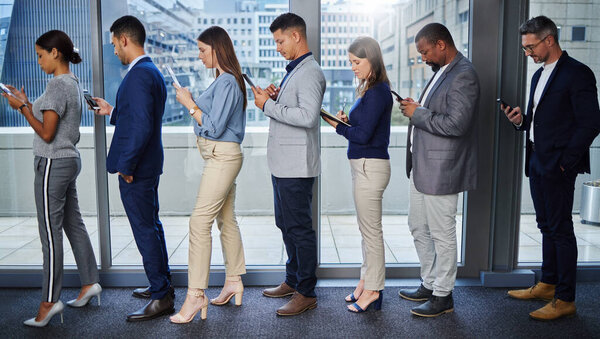 Success comes from preparation. Shot of a group of young businesspeople using digital devices while waiting in line.