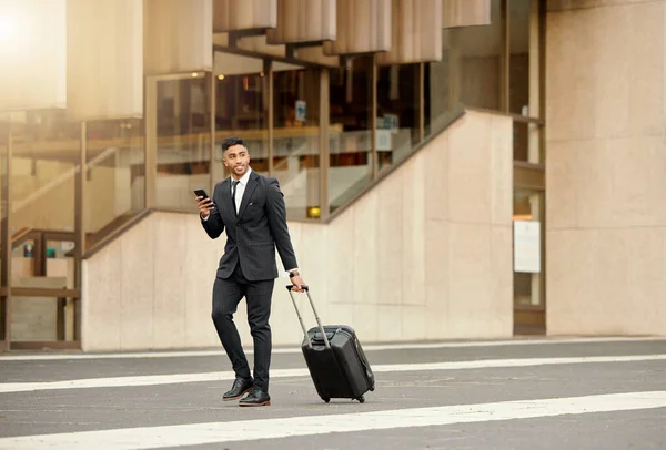 Será mejor que tengan detalles de vuelo. Disparo de un hombre de negocios caminando por la ciudad con su equipaje usando su teléfono inteligente. — Foto de Stock