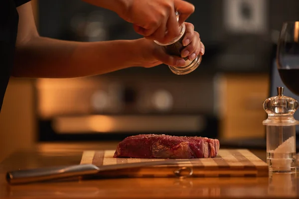 Vlees moet altijd goed gekruid zijn. Shot van een vrouw kruiden van een stuk steak voor het diner. — Stockfoto