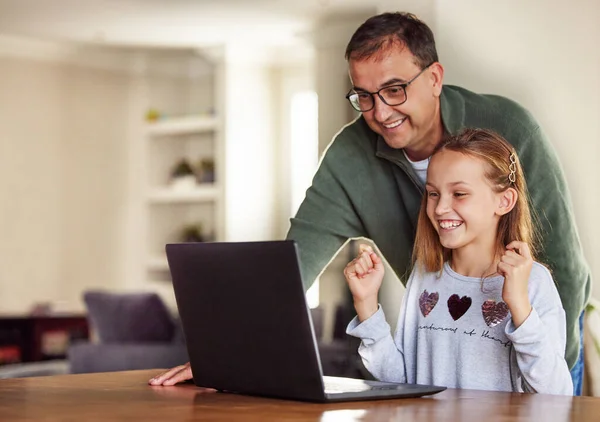 Ik ben geslaagd voor mijn huisschool examens. Shot van een schattig klein meisje zitten en met behulp van een laptop thuis, terwijl haar vader helpt haar. — Stockfoto