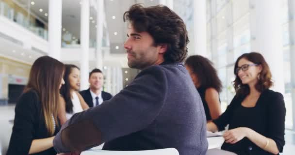 Wir arbeiten immer als eingespieltes Team. 4k-Videoaufnahmen eines jungen Geschäftsmannes, der während eines Treffens mit seinen Kollegen im Hintergrund in einem Büro lächelt. — Stockvideo