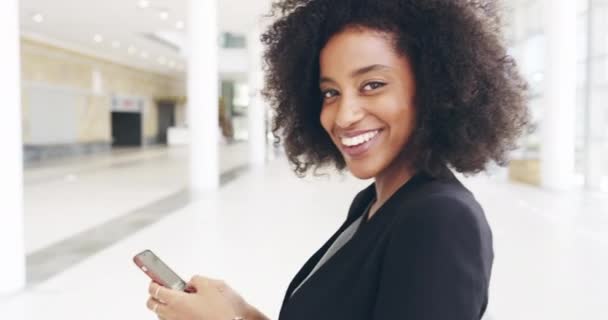 Verbindingen maken met draadloze technologie. 4k video beelden van een aantrekkelijke jonge zakenvrouw met behulp van haar mobiele telefoon terwijl staan in het kantoor. — Stockvideo