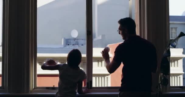 Single dads are superheroes. 4k video footage of a little girl cleaning windows with her father at home. — ストック動画