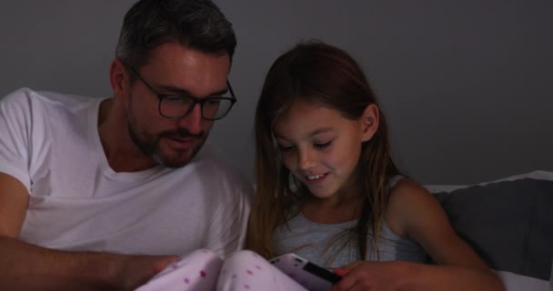 Its not bedtime without a bedtime story. 4k video footage of a cute little girl using a digital tablet with her father at bedtime. — стоковое видео