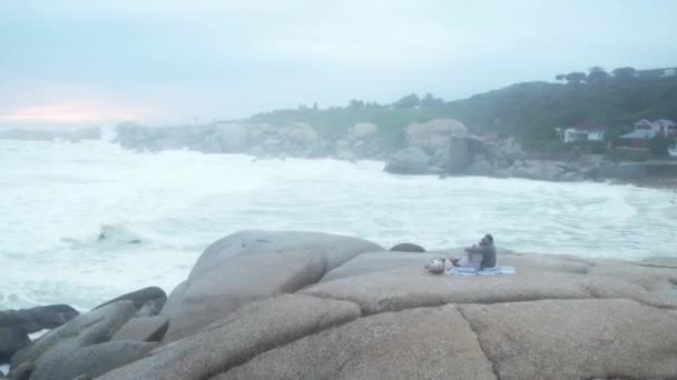 This is our most favorite spot to come to. Aerial drone footage of a mature couple having a picnic on rocks along the beach. — Stock video