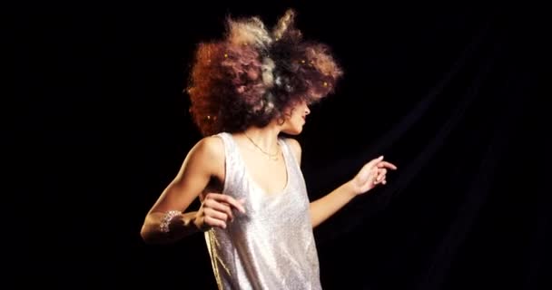 Mulher afro-americana despreocupada dançando contra um fundo preto com confete dourado em seu cabelo. Jovem mulher se divertindo em uma festa celebrando e dançando contra um fundo escuro — Vídeo de Stock