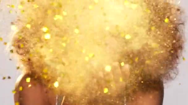 Beautiful african american woman with an afro at a party blowing gold glitter and confetti from her hands.Happy young woman having fun blowing gold confetti and sparkles from her hands. — Stock video